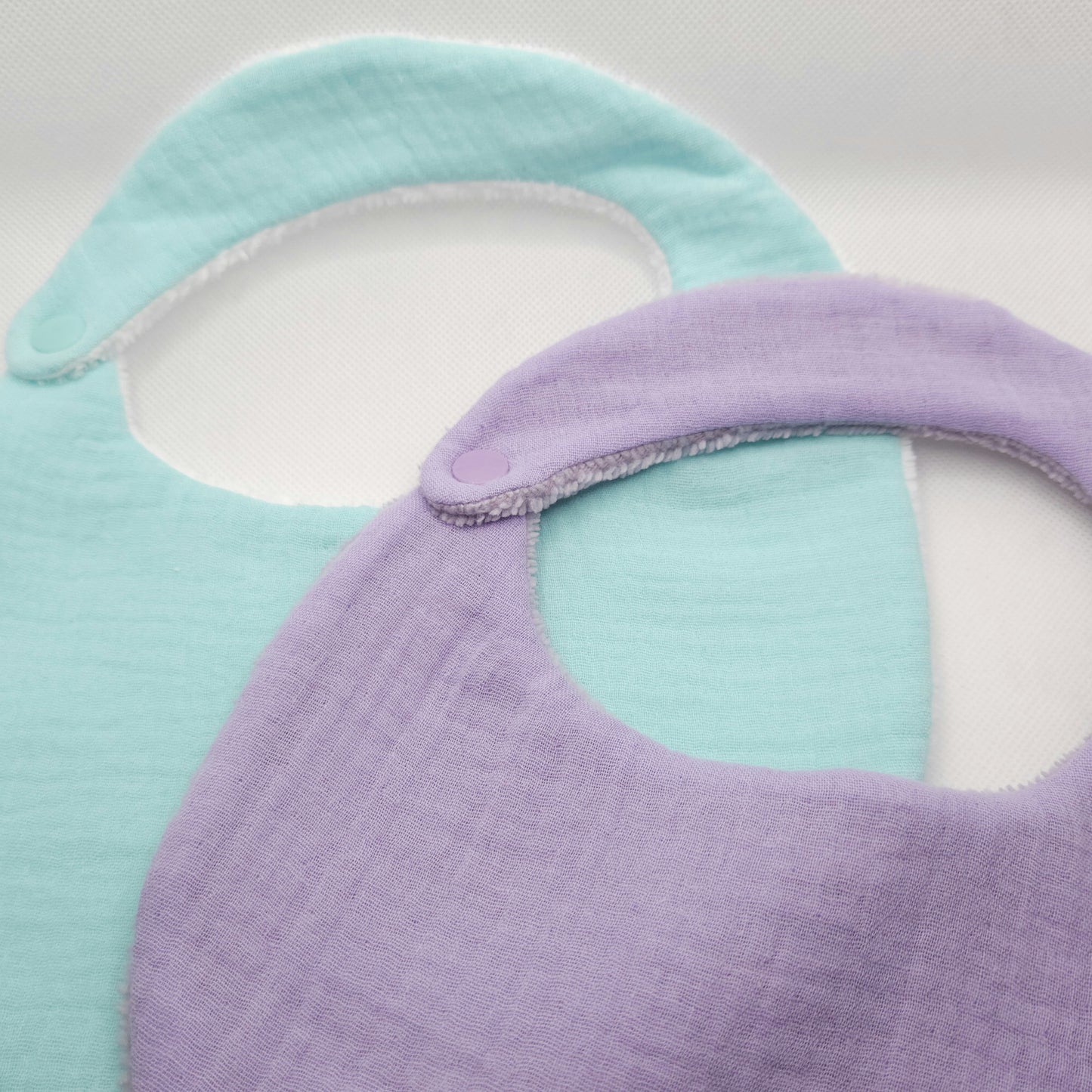 Two baby bibs, one purple and one light blue, on a white background.