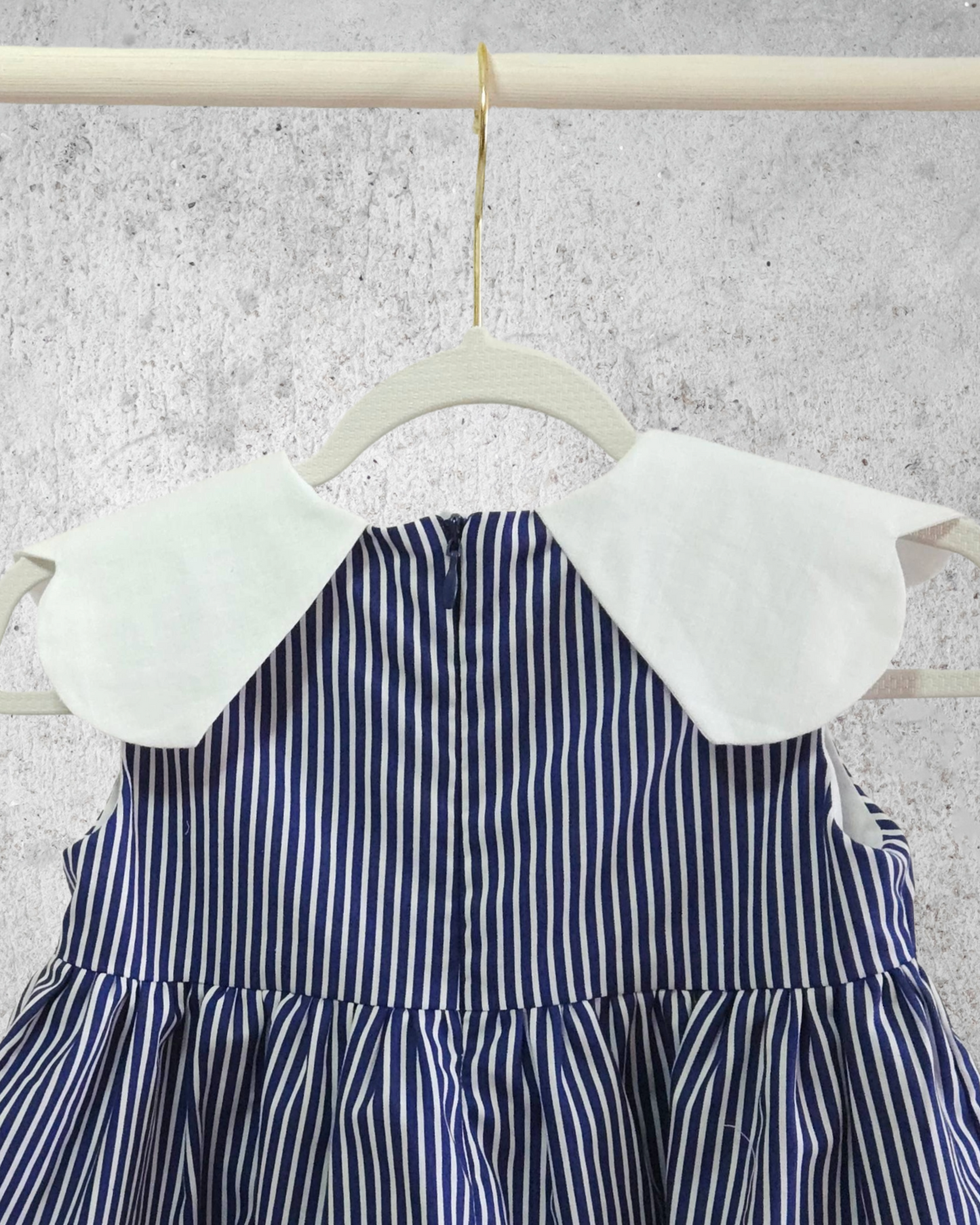 Blue and white striped dress with a white collar on a hanger against a gray background