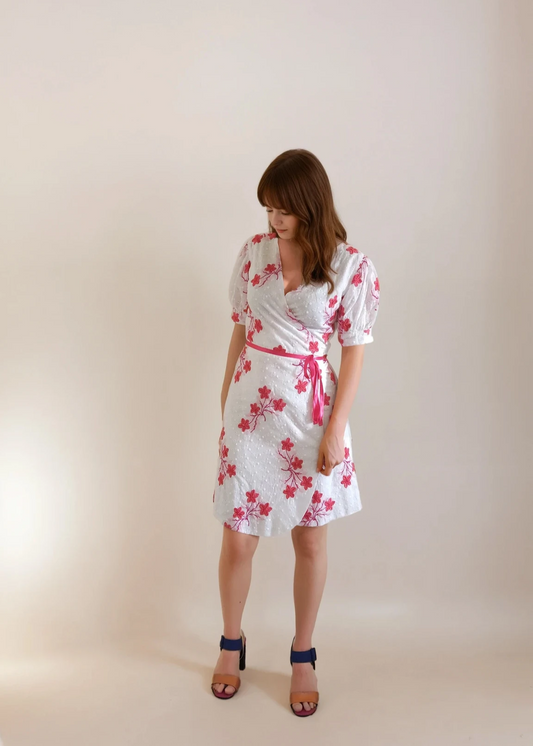 Woman wearing a white wrap over dress with pink floral embroderies against a plain background