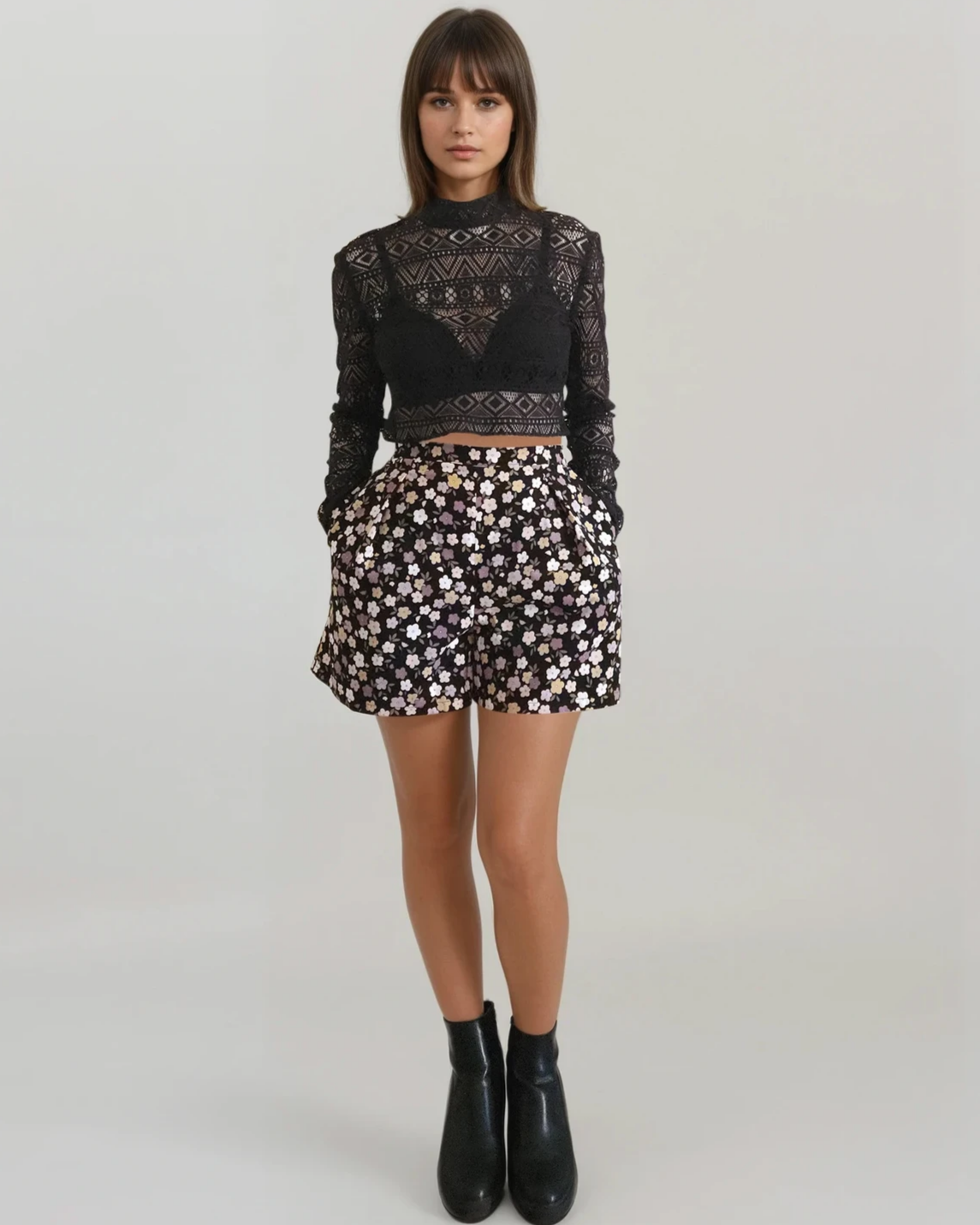 Woman wearing a black lace top and floral short on a plain background