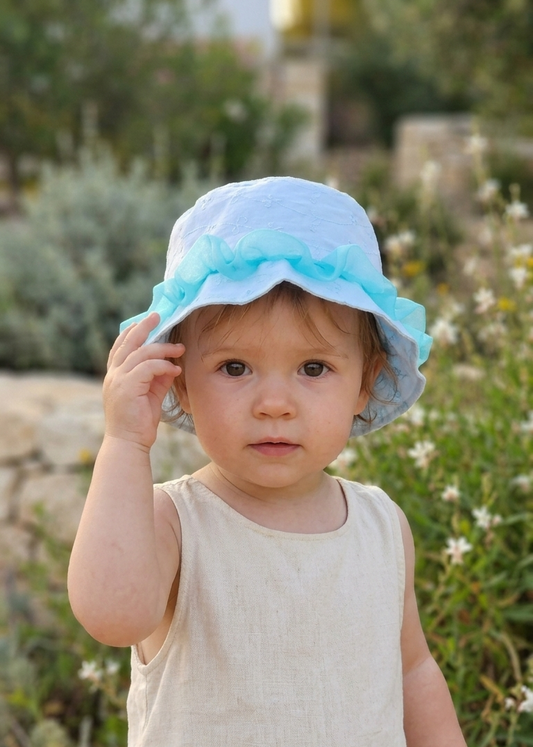 Child wearing a light blue hat outdoors with greenery in the background