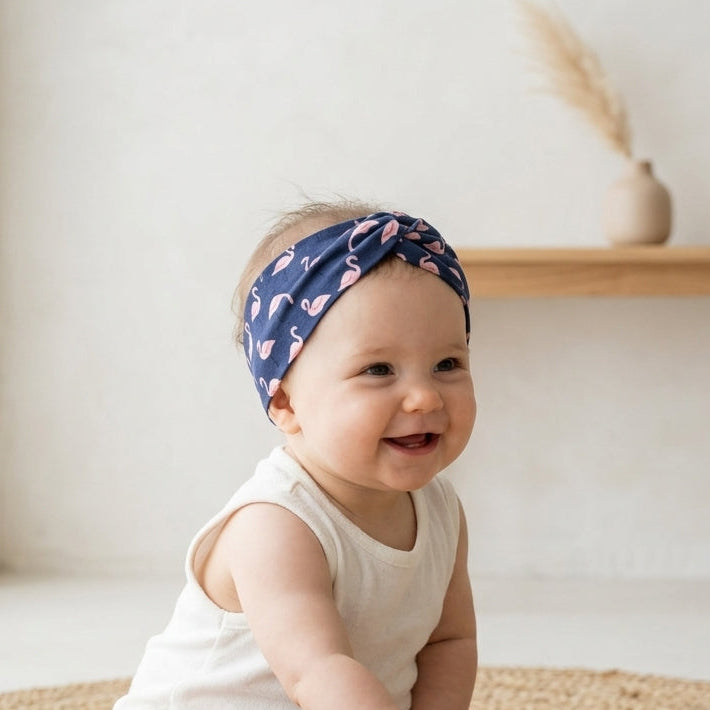 Baby sitting on a woven mat wearing a navy handmade headband with flamingo