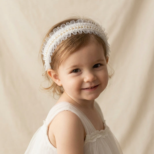 Child wearing a white headband with pearls and tulle embellishment against a beige background