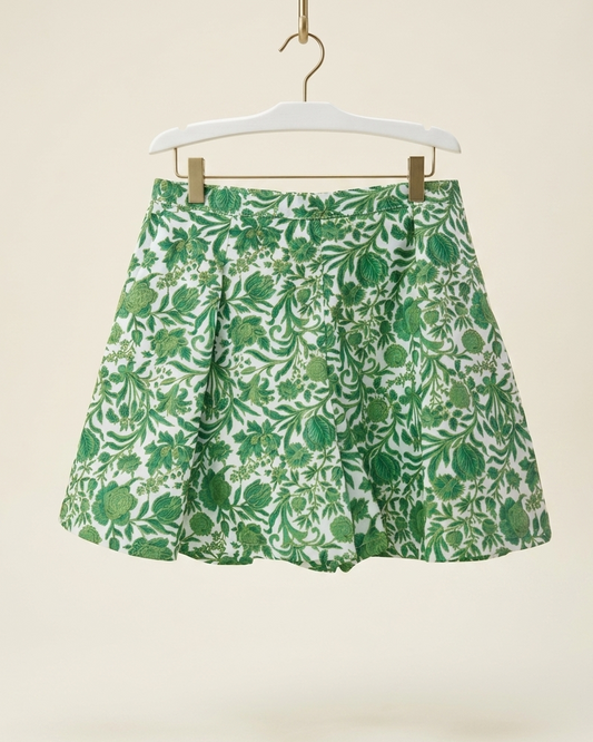 Green and Golden floral print pleated Short hanging on a white hanger with gold clips against a warm beige background.