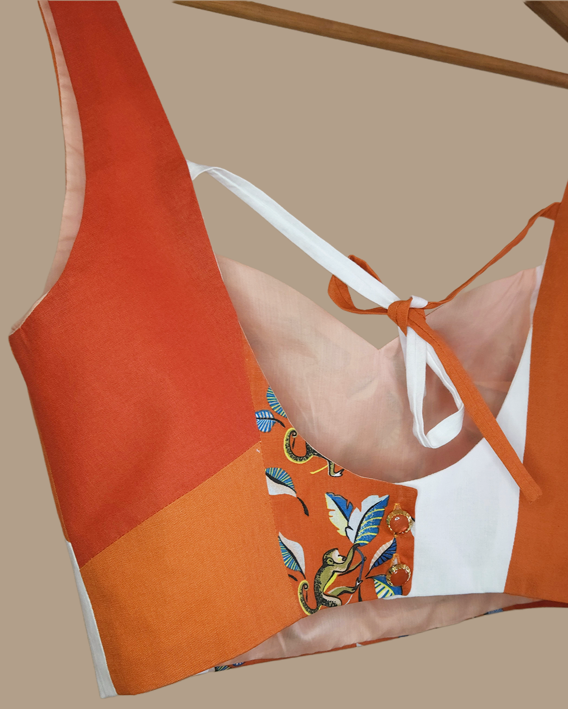 A close-up of a women's blouse with a patchwork design. The fabric includes solid orange sections, a white side panel, and a central monkey print panel 