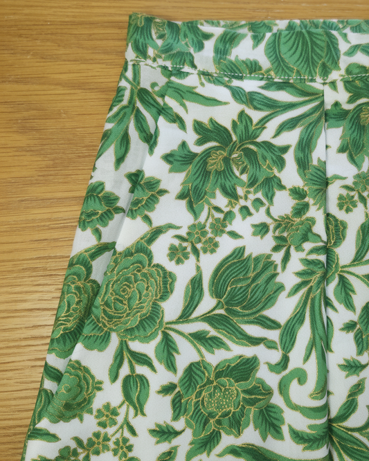 A close-up of the side pocket of the short featuring a green and gold floral pattern, laid flat on a light brown wooden surface.