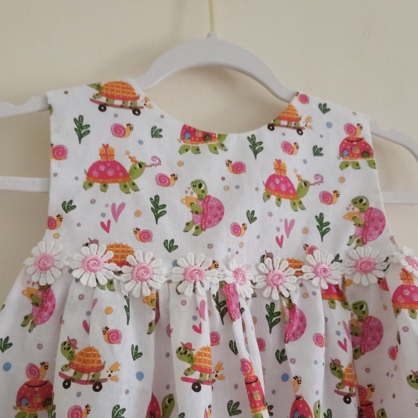Children's dress with turtle and flower pattern on a hanger against a beige wall.